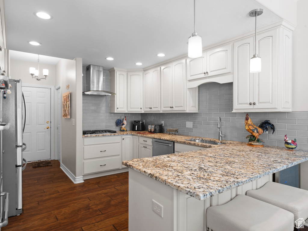 Kitchen with wall chimney exhaust hood, a sink, a peninsula, appliances with stainless steel finishes, and dark wood-style flooring