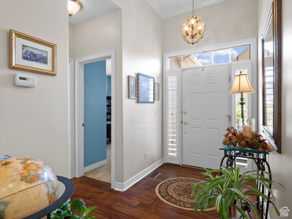 Entryway with dark wood-style flooring, a chandelier, baseboards, and ornamental molding