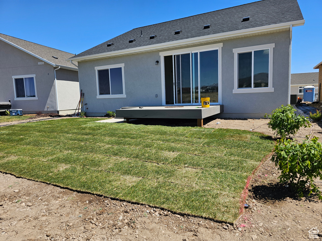 Rear view of property with a lawn, a shingled roof, and stucco siding