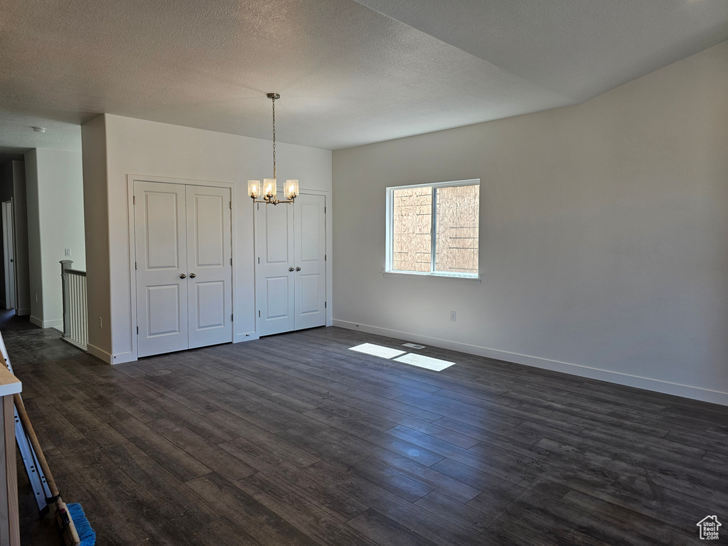 Unfurnished dining area with a chandelier, baseboards, dark wood-style flooring, and a textured ceiling