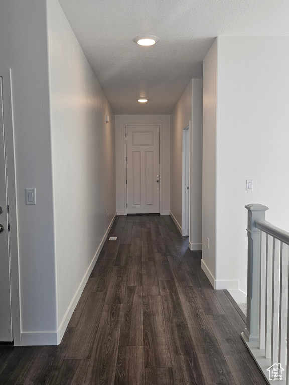 Corridor featuring dark wood-type flooring, baseboards, a textured ceiling, and an upstairs landing