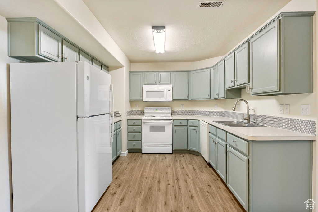 Kitchen with white appliances, a sink, light wood-style flooring, and light countertops