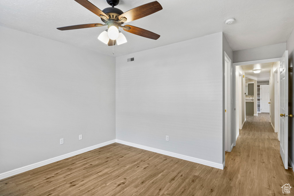 Spare room with light wood-type flooring, baseboards, a ceiling fan, and a smoke detector
