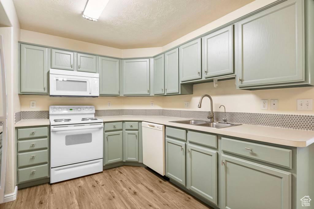 Kitchen featuring white appliances, a sink, green cabinets, light wood-style flooring, and light countertops