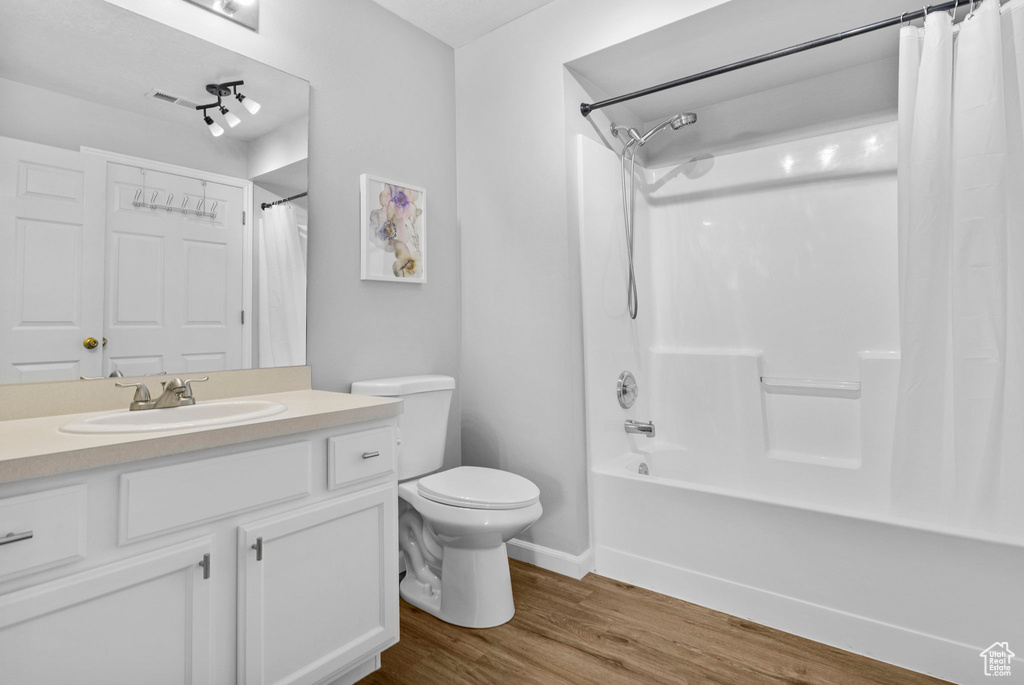 Full bath with wood finished floors, toilet, shower / tub combo with curtain, vanity, and baseboards