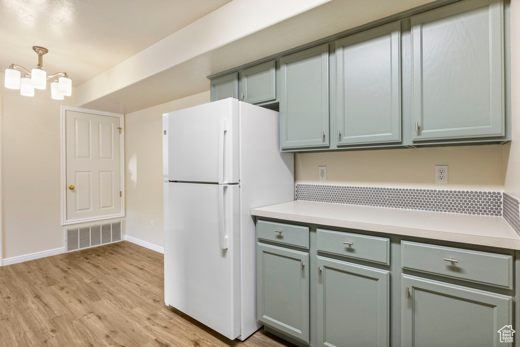 Kitchen with freestanding refrigerator, light countertops, light wood-style floors, baseboards, and a chandelier
