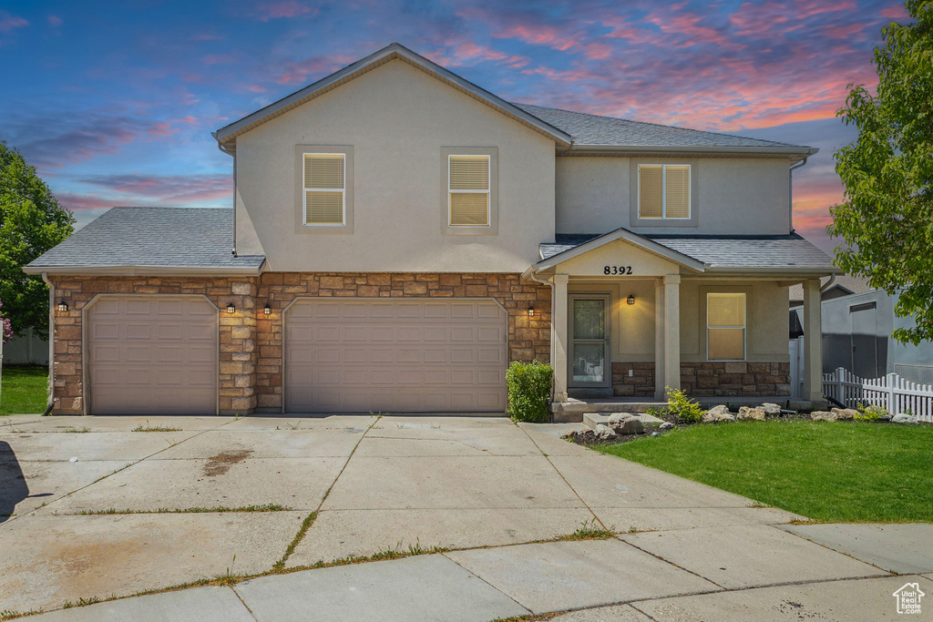 View of front of property with stone siding, concrete driveway, stucco siding, covered porch, and an attached garage