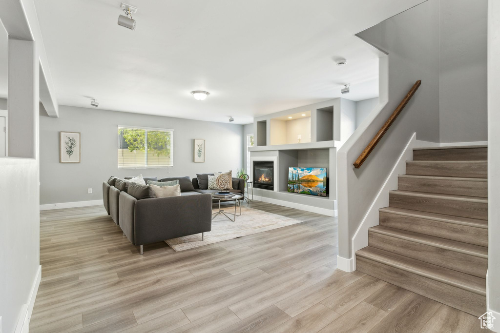 Living room featuring baseboards, a glass covered fireplace, stairway, and light wood-type flooring