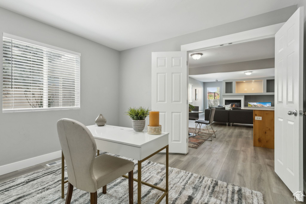 Office space with light wood-style flooring, baseboards, and a glass covered fireplace