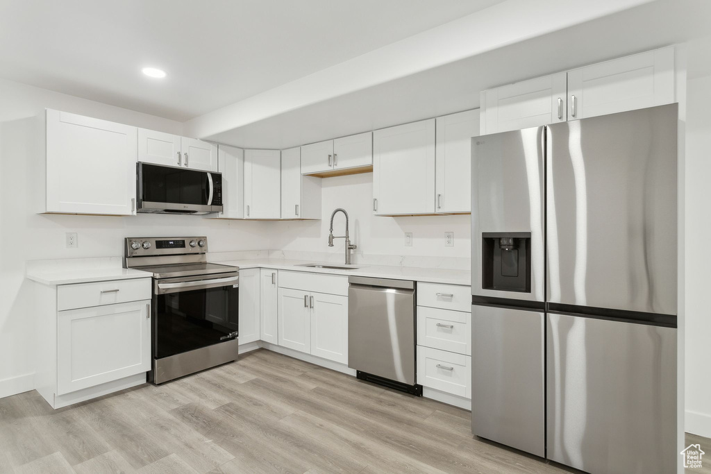 Kitchen with stainless steel appliances, a sink, recessed lighting, light countertops, and white cabinets