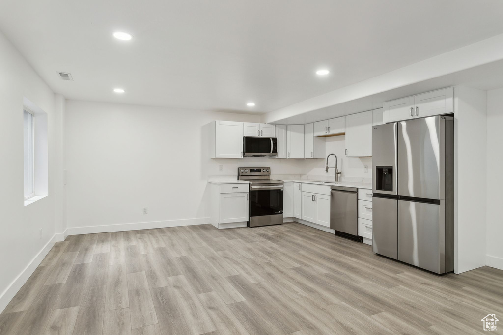 Kitchen with stainless steel appliances, light countertops, recessed lighting, light wood finished floors, and white cabinets