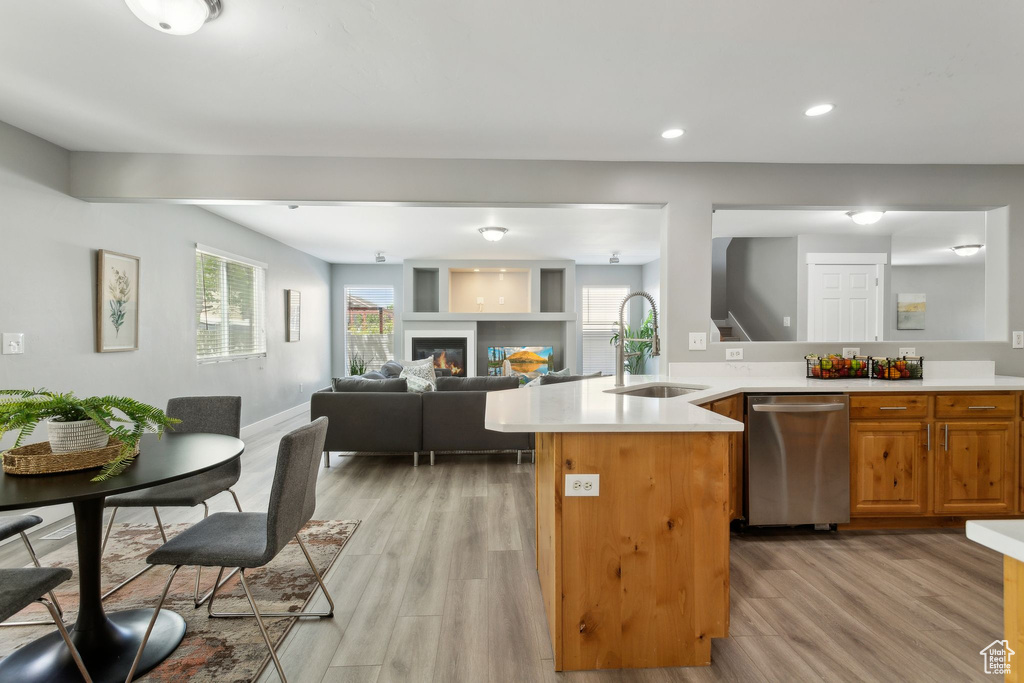 Kitchen featuring a sink, stainless steel dishwasher, light wood-style floors, light countertops, and healthy amount of natural light