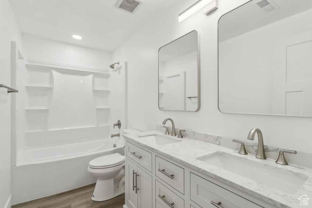 Full bathroom featuring wood finished floors, toilet, double vanity, washtub / shower combination, and recessed lighting
