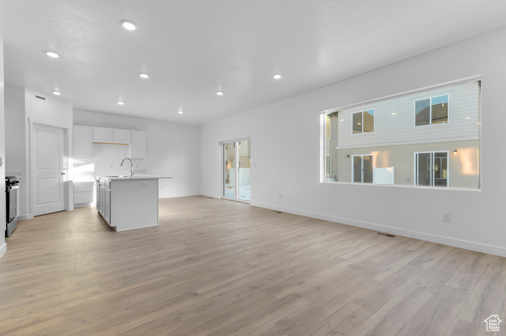 Unfurnished living room featuring recessed lighting, light wood-type flooring, baseboards, and a sink