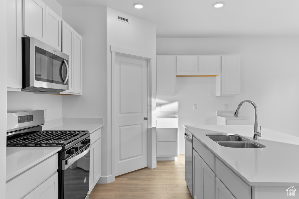 Kitchen with stainless steel appliances, light wood-style flooring, a sink, white cabinetry, and recessed lighting