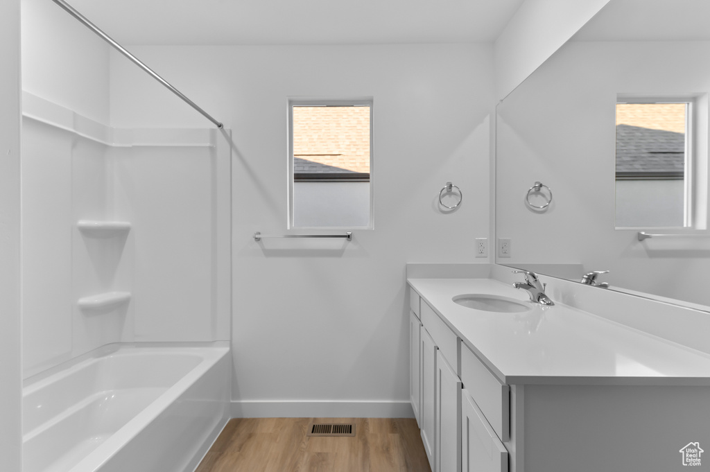Full bath with baseboards, wood finished floors, vanity, and shower / bath combination