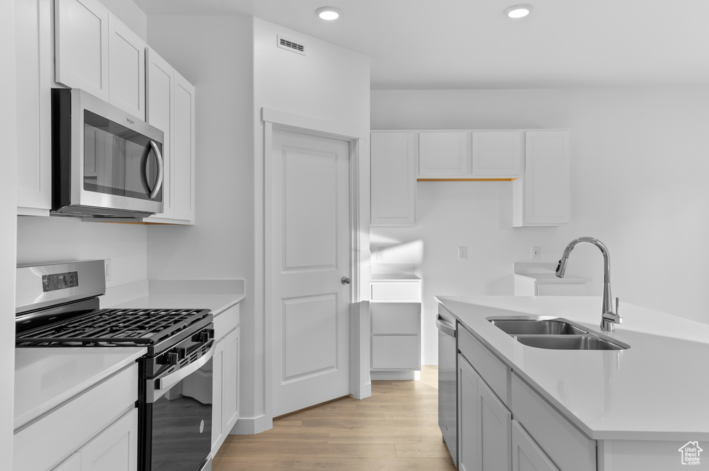 Kitchen featuring stainless steel appliances, light wood-style floors, a sink, white cabinets, and recessed lighting