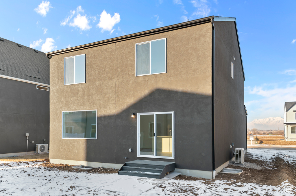 Snow covered rear of property with ac unit and stucco siding