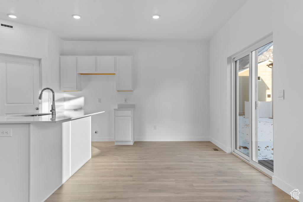 Kitchen with a sink, white cabinetry, light wood-style floors, recessed lighting, and baseboards