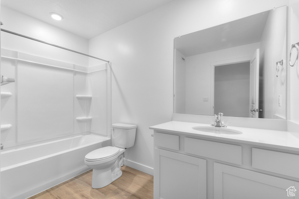 Full bathroom with wood finished floors, toilet, vanity, baseboards, and tub / shower combination
