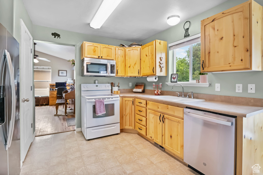 Kitchen with appliances with stainless steel finishes, light brown cabinetry, a sink, light countertops, and lofted ceiling