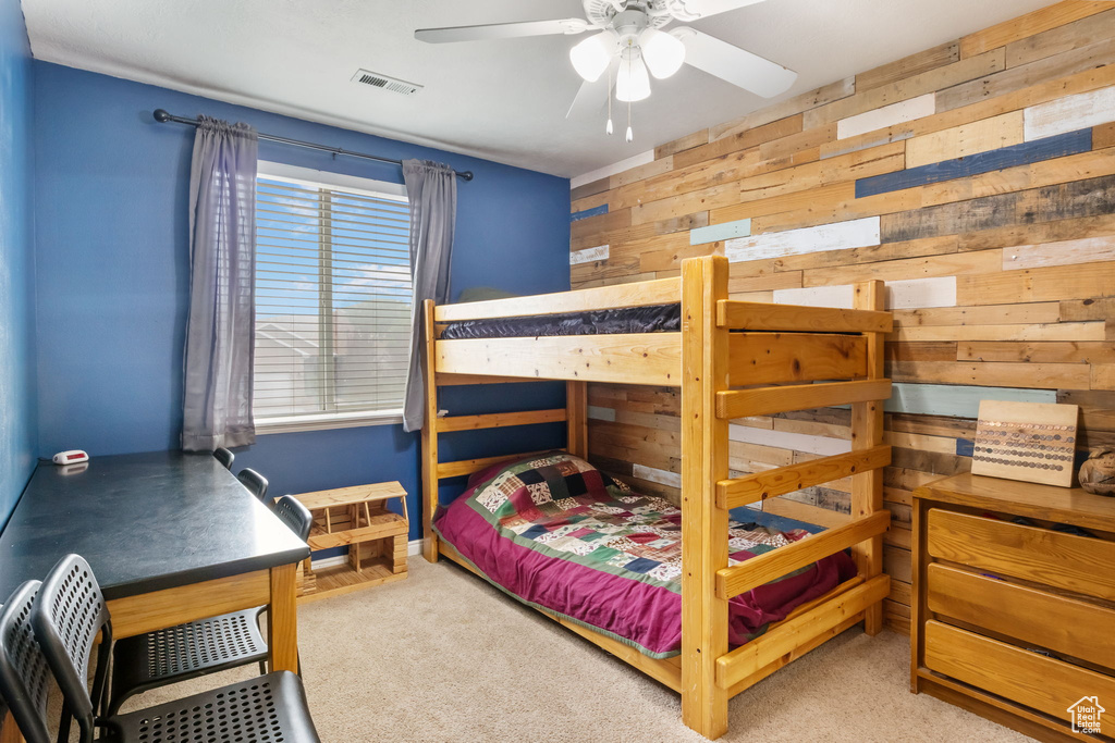 Carpeted bedroom featuring wood walls and a ceiling fan