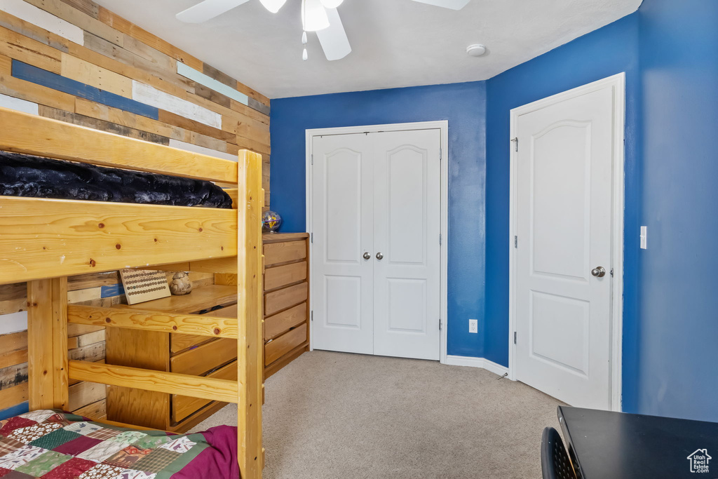 Carpeted bedroom featuring a closet, a ceiling fan, baseboards, and wooden walls