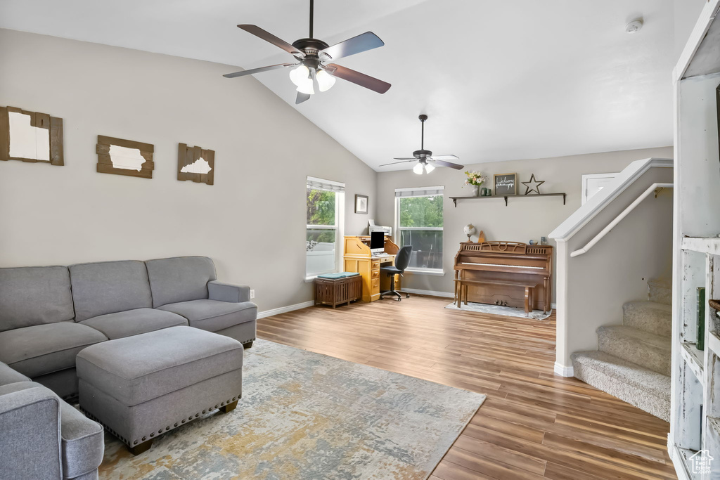 Living room featuring ceiling fan, stairway, baseboards, wood finished floors, and vaulted ceiling