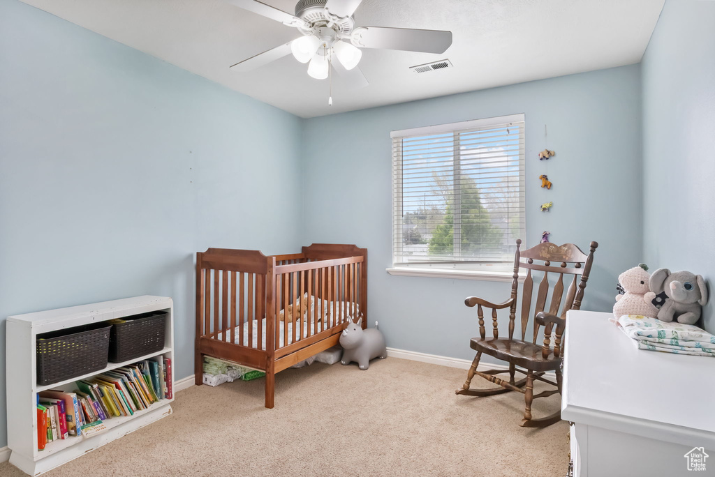 Carpeted bedroom with baseboards, a nursery area, and a ceiling fan