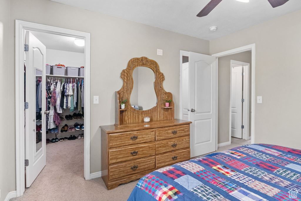 Bedroom with a walk in closet, light colored carpet, a closet, baseboards, and a ceiling fan