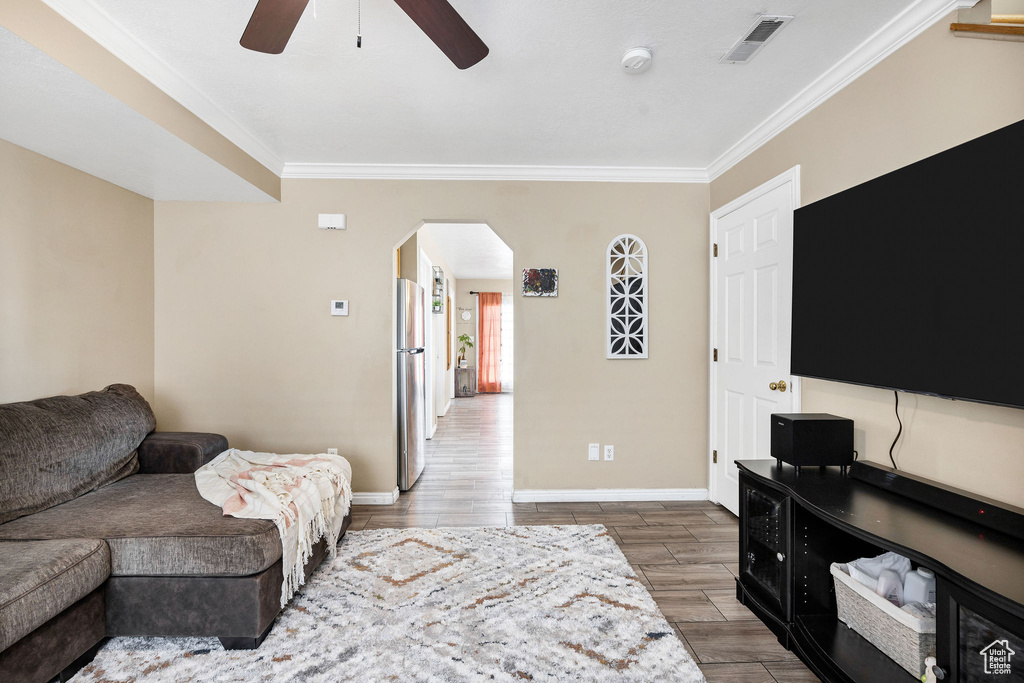 Living room featuring arched walkways, ornamental molding, a ceiling fan, baseboards, and wood finished floors