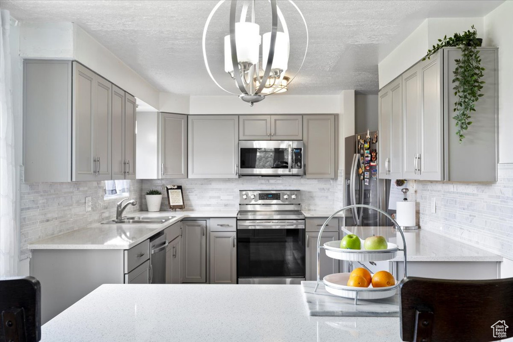 Kitchen with gray cabinetry, stainless steel appliances, a sink, a chandelier, and backsplash