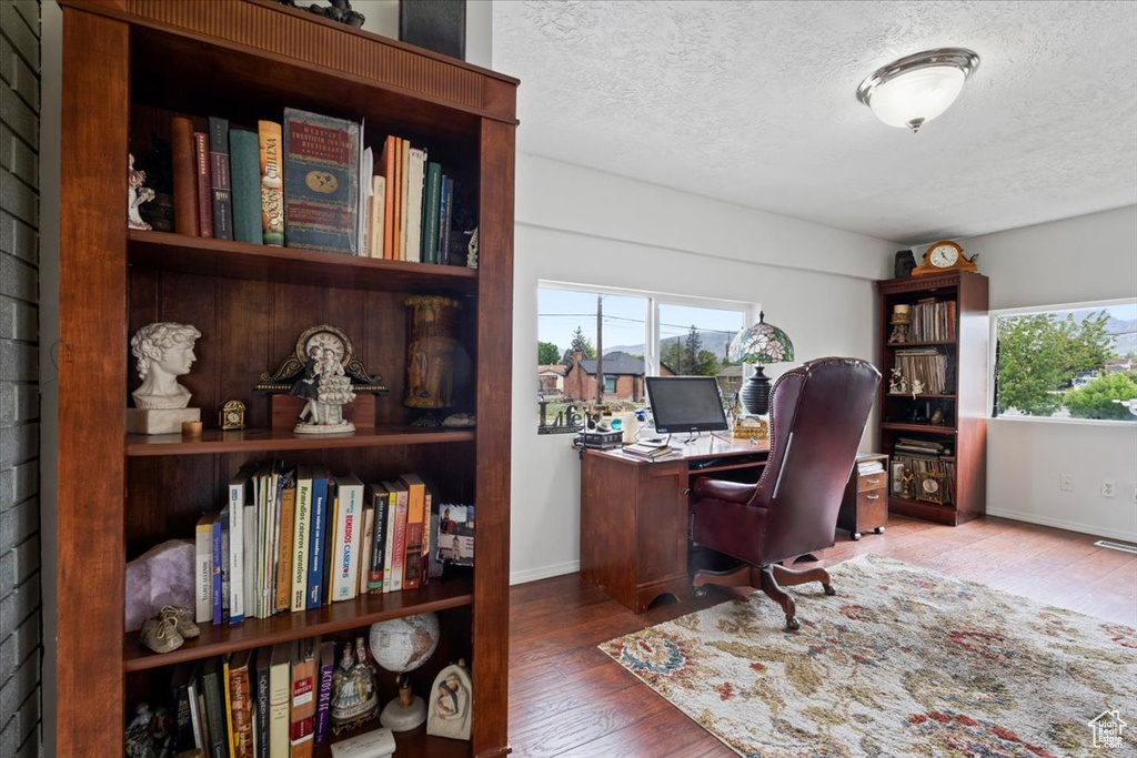 Office with a textured ceiling, healthy amount of natural light, wood finished floors, and baseboards