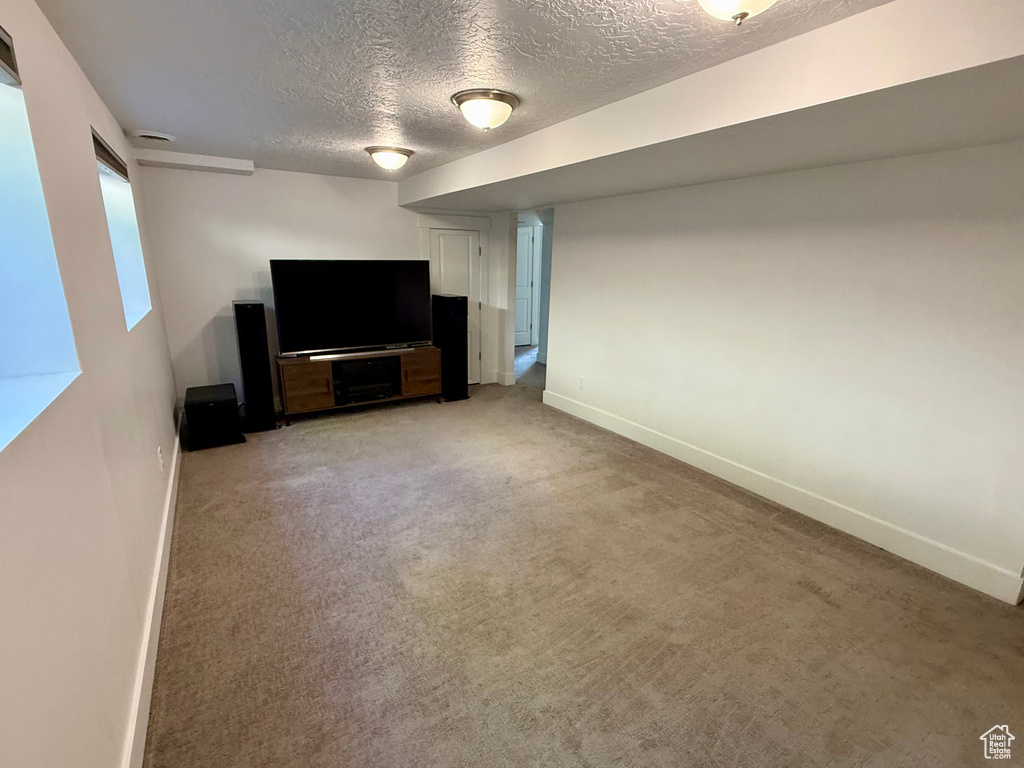 Unfurnished living room with a textured ceiling, baseboards, and light carpet