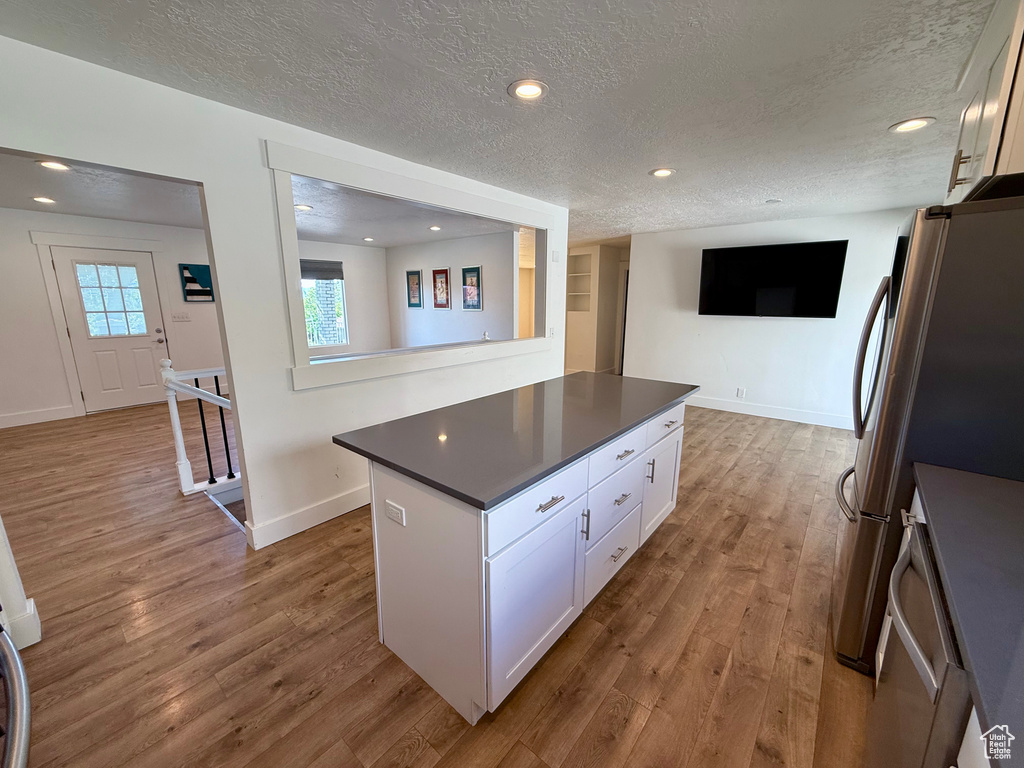 Kitchen featuring a textured ceiling, dark countertops, white cabinetry, wood finished floors, and freestanding refrigerator