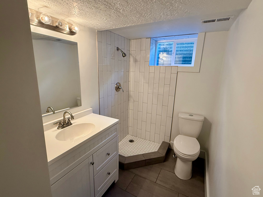 Bathroom with toilet, a textured ceiling, tile patterned floors, vanity, and tiled shower