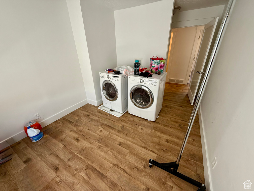 Washroom with independent washer and dryer, light wood finished floors, and baseboards