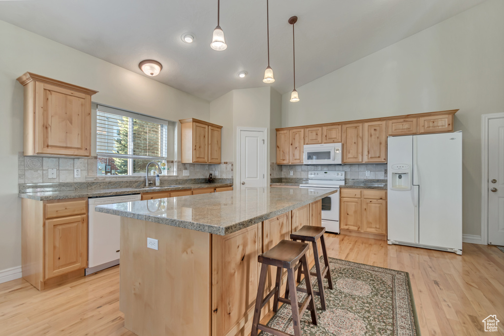 Kitchen featuring white appliances, light wood-type flooring, high vaulted ceiling, a center island, and tasteful backsplash