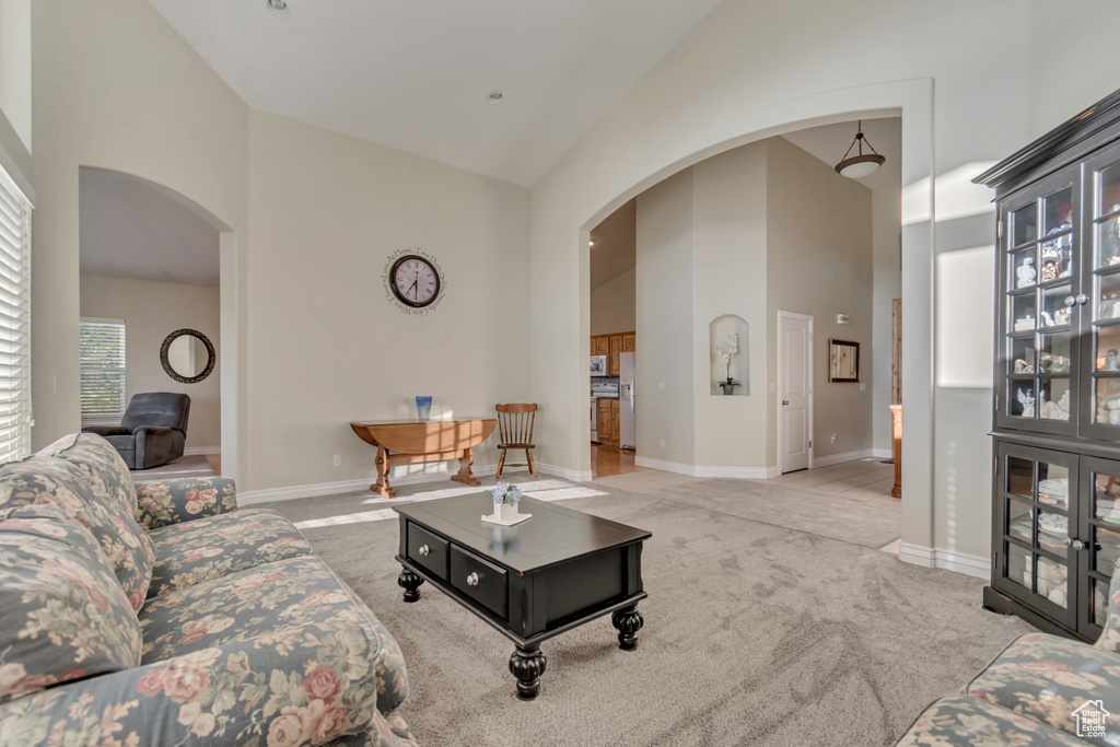 Carpeted living area featuring arched walkways, high vaulted ceiling, and baseboards