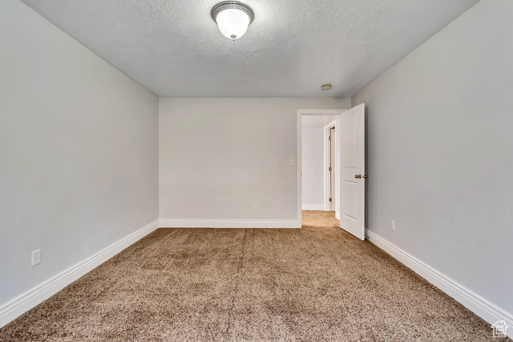 Empty room with carpet floors, a textured ceiling, and baseboards