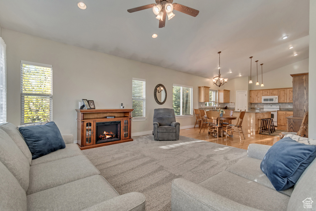 Living room featuring ceiling fan, baseboards, a lit fireplace, a chandelier, and lofted ceiling