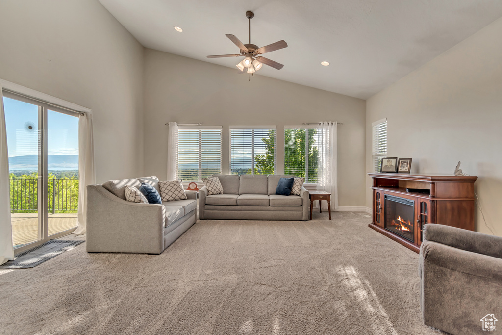 Carpeted living area with a ceiling fan, a glass covered fireplace, high vaulted ceiling, and recessed lighting