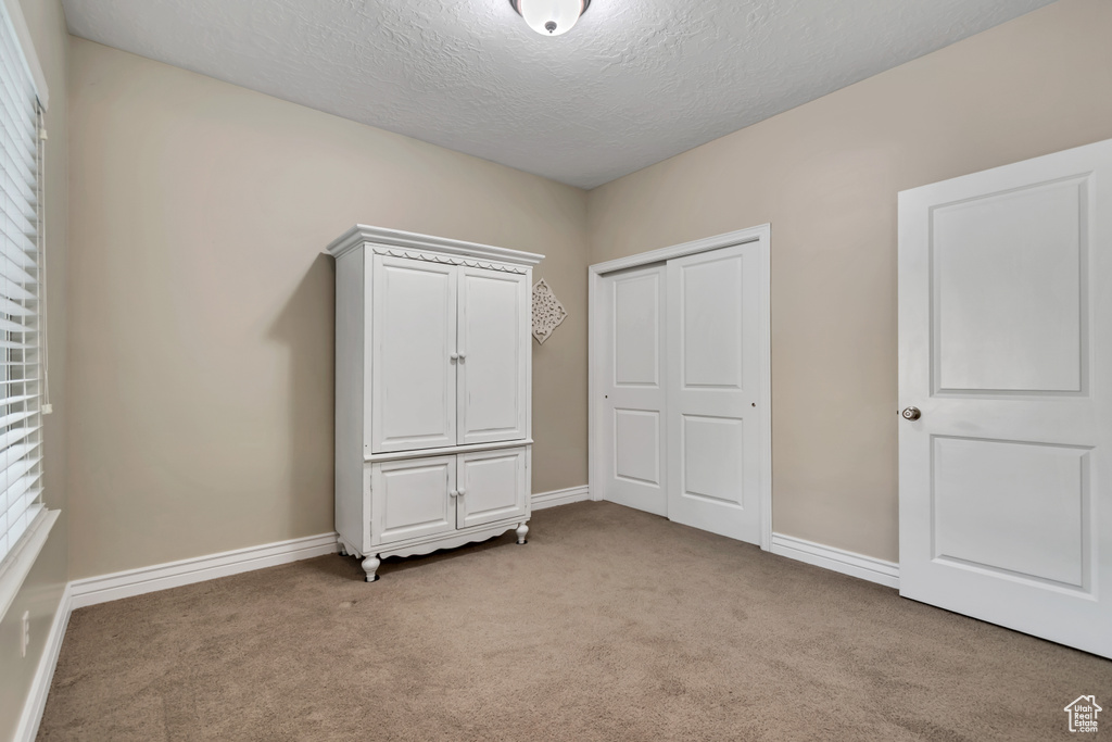 Unfurnished bedroom featuring light carpet, a textured ceiling, a closet, and baseboards
