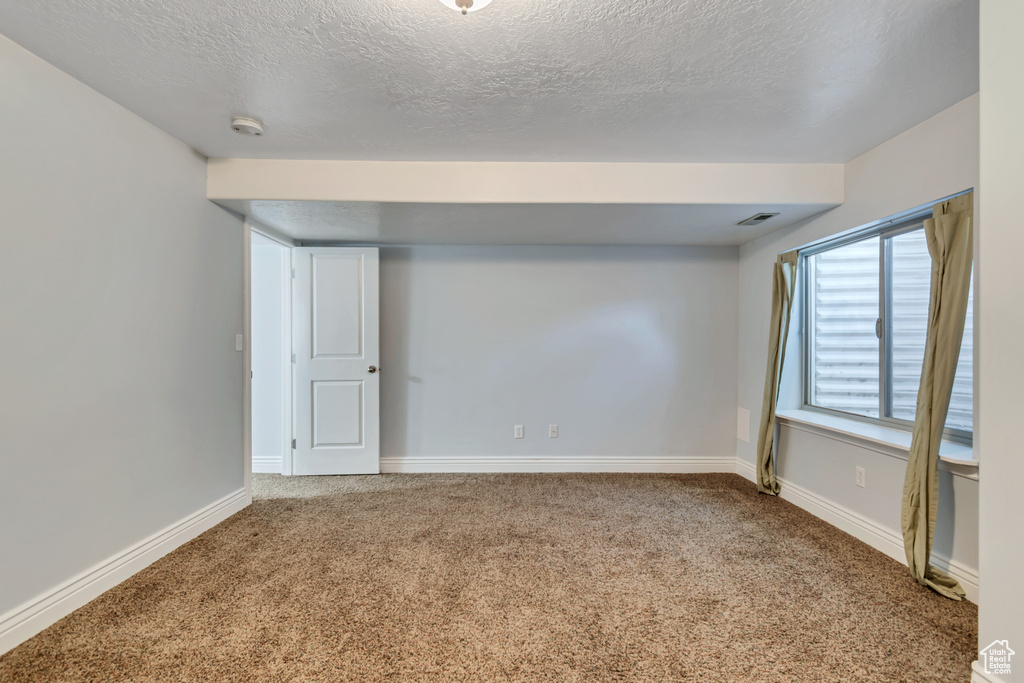 Carpeted empty room featuring a textured ceiling and baseboards