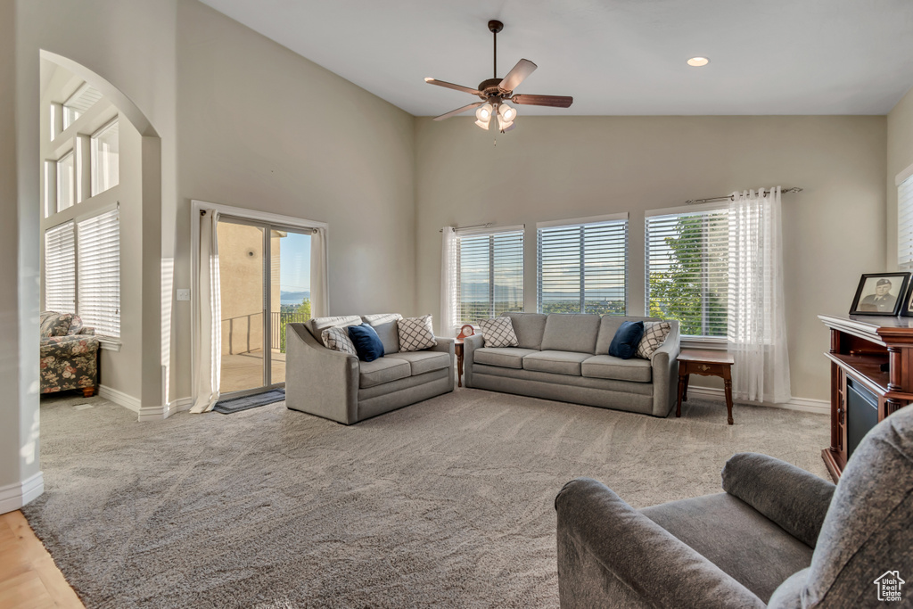 Living area with plenty of natural light, a ceiling fan, high vaulted ceiling, baseboards, and carpet flooring