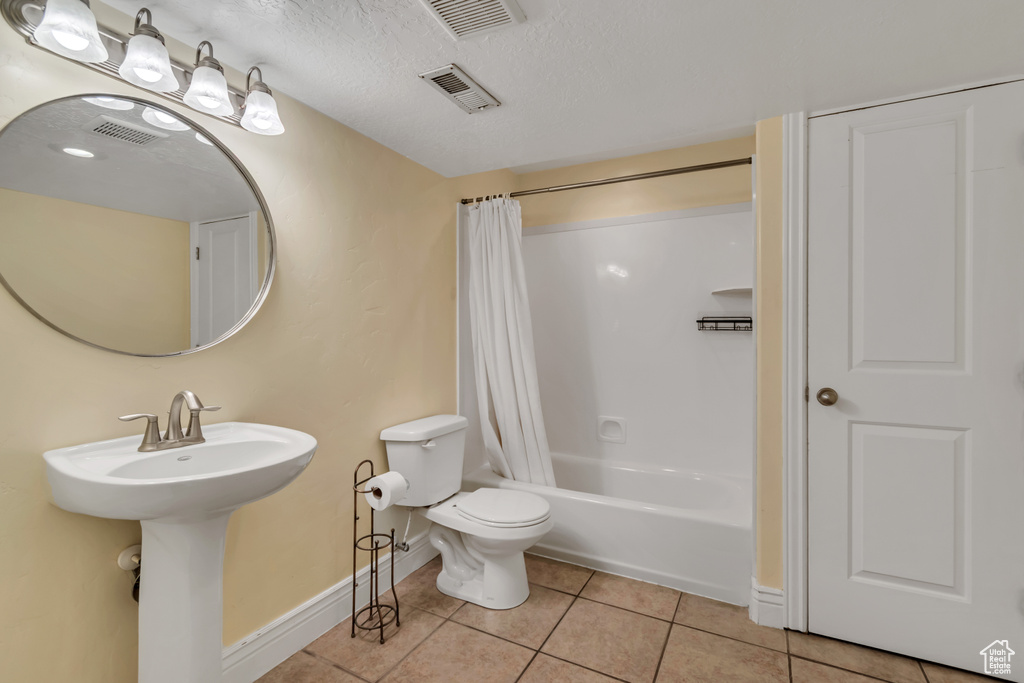 Bathroom with baseboards, tile patterned flooring, toilet, shower / tub combo, and a sink