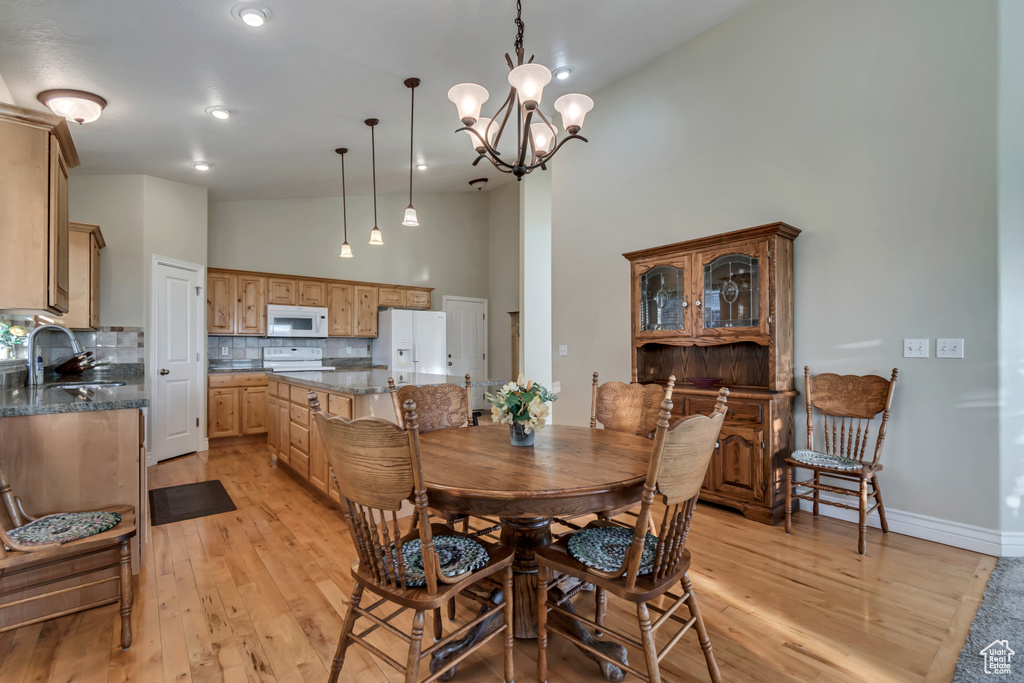 Dining area with light wood finished floors, a high ceiling, a chandelier, and baseboards