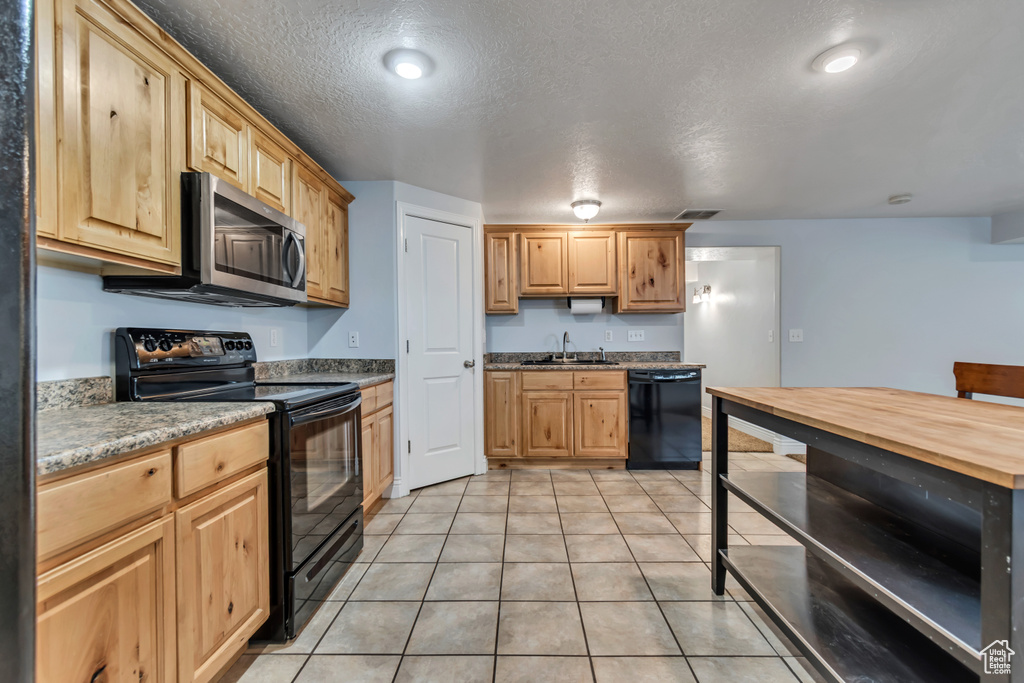 Kitchen featuring black appliances, a sink, light tile patterned flooring, light brown cabinetry, and a textured ceiling