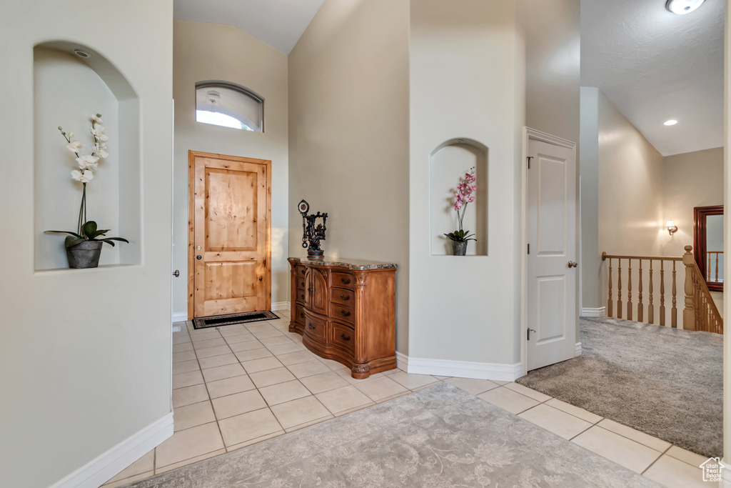 Foyer with light tile patterned floors, baseboards, lofted ceiling, and light carpet