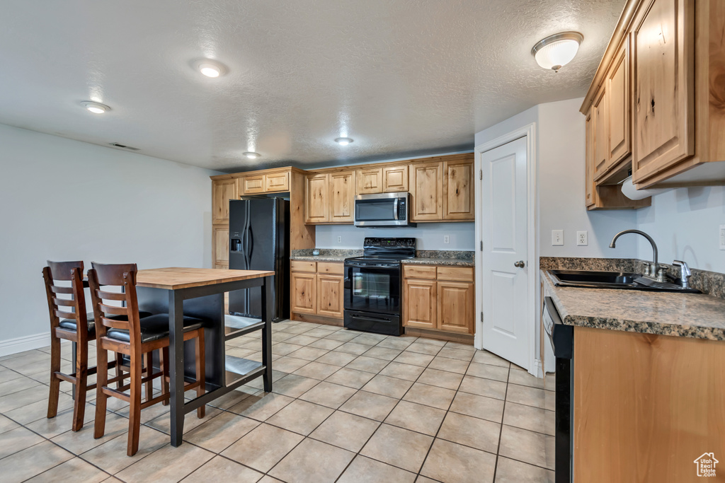 Kitchen with black appliances, a sink, light tile patterned floors, and a textured ceiling